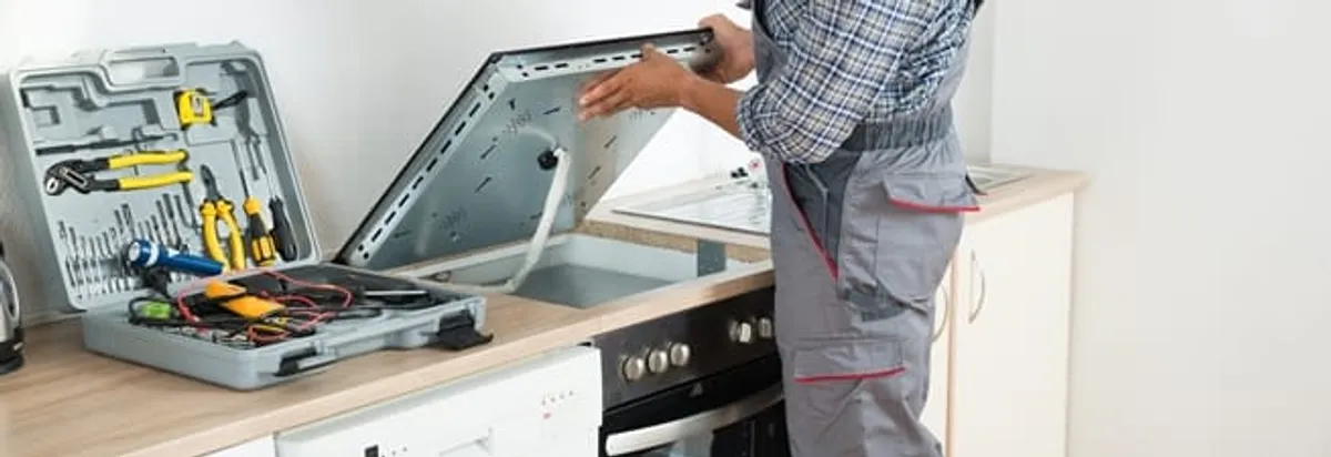 Cooktop repair technician lifting a built-in stovetop for service in Columbia, MO