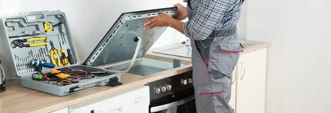 Cooktop repair technician lifting a built-in stovetop for service in Columbia, MO