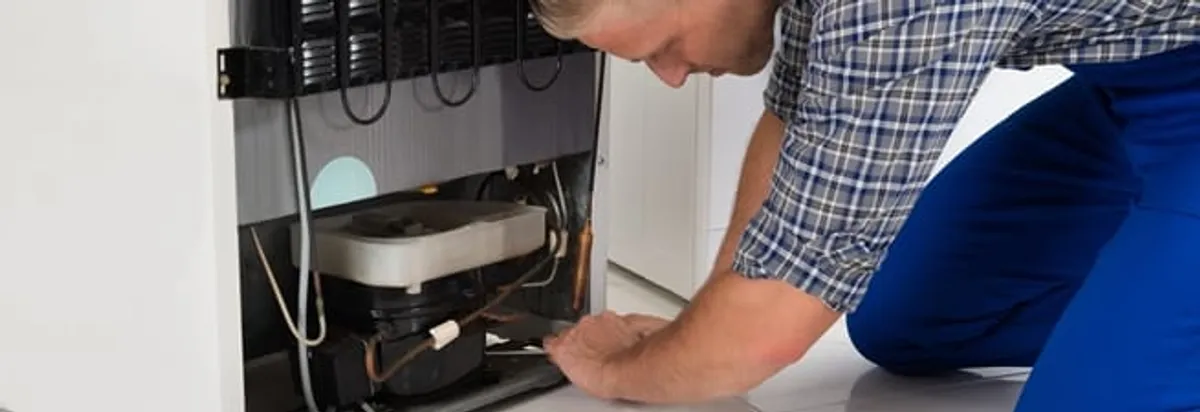 Refrigerator repair technician servicing the compressor and condenser area in Columbia, MO