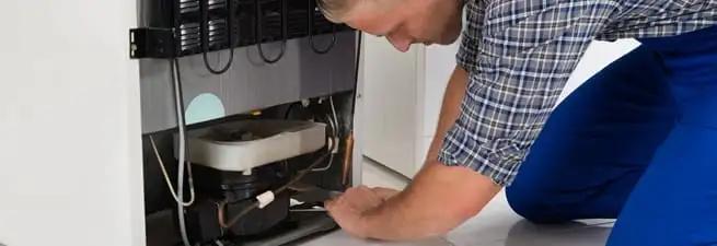 Refrigerator repair technician servicing the compressor and condenser area in Columbia, MO