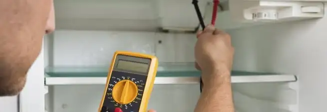 Refrigerator repair technician testing electrical components with a multimeter in Columbia, MO