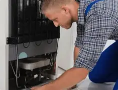 Refrigerator repair technician servicing the compressor and condenser area in Columbia, MO
